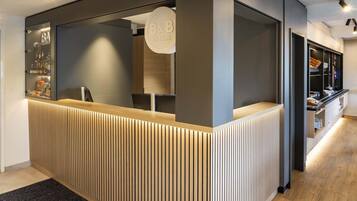 A reception desk with a modern design, featuring a wooden slatted front panel and a glass enclosure with a sign.