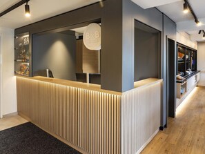 Un mostrador de recepción con diseño moderno, que presenta un panel frontal de listones de madera y una estructura de vidrio con un cartel.