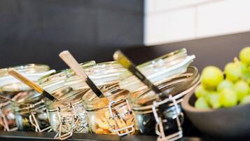 Montaje de buffet con diversos alimentos en recipientes de vidrio y un tazón de manzanas verdes.