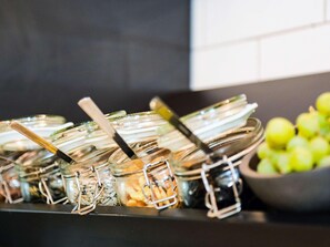 Montaje de buffet con diversos alimentos en recipientes de vidrio y un tazón de manzanas verdes.