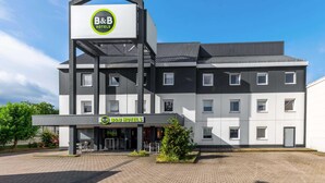 Un hotel B&B con diseño moderno, que presenta un logotipo destacado en la fachada, amplias ventanas y un área de entrada pavimentada.