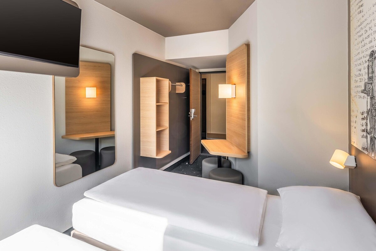 A modern hotel room with a bed, bedside tables, a mirror, and built-in shelving.
