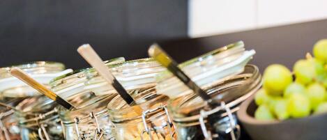 Montaje de buffet con diversos alimentos en recipientes de vidrio y un tazón de manzanas verdes.