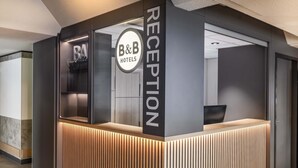 Una zona de recepción de diseño moderno, con mostrador de recepción, separador de vidrio y un cartel de B&B Hotels.