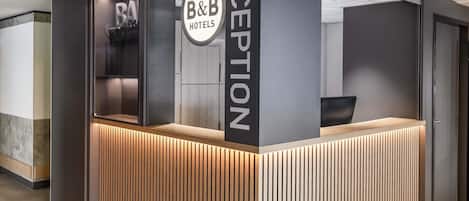 A reception area with a modern design, including a reception desk, a glass partition, and a sign for B&B Hotels.