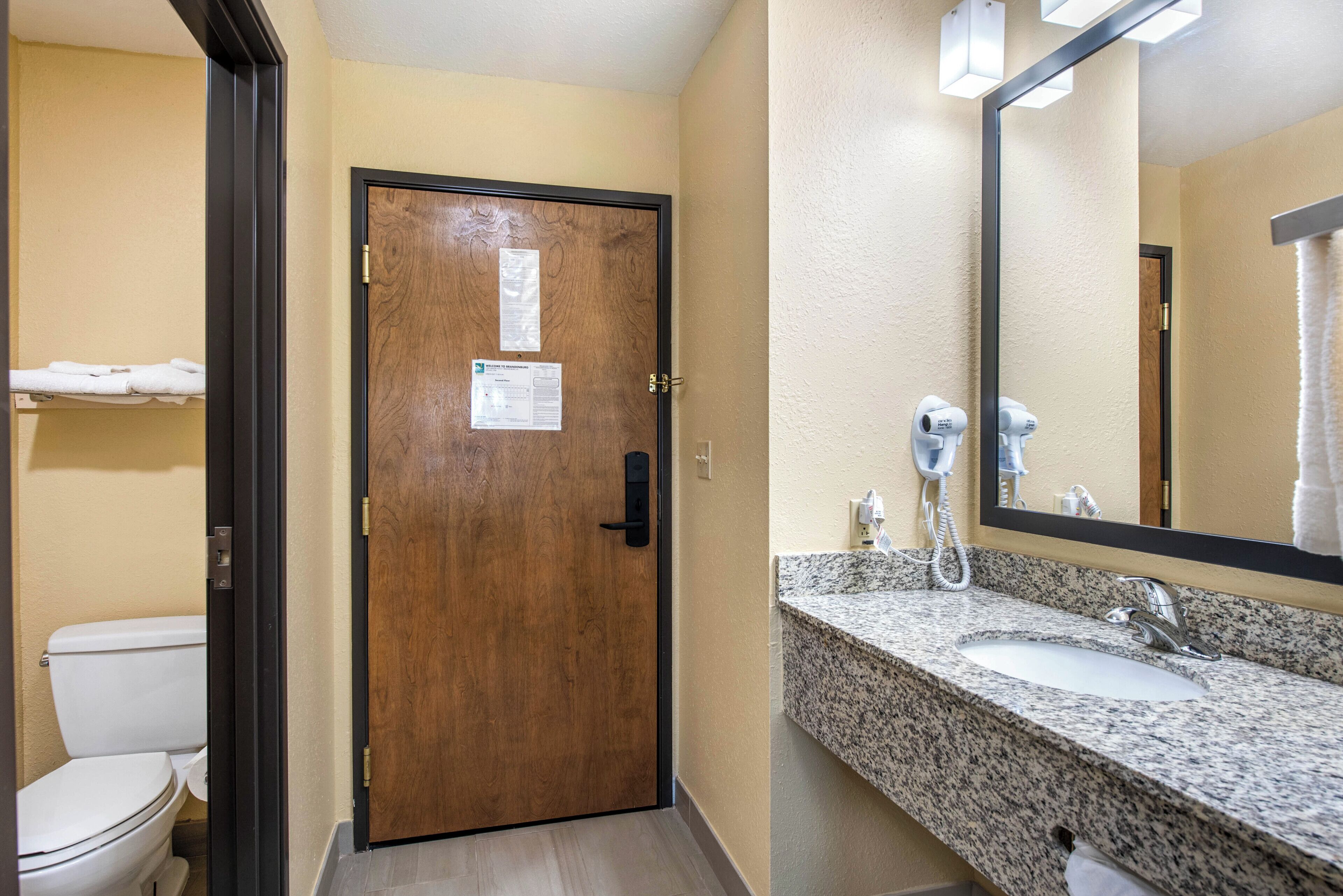 A bathroom with a wooden door, a white toilet, a granite sink, and a mirror.