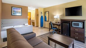 Habitación de hotel con una cama grande, un sofá, un escritorio con una silla, microondas, televisor y baño con bañera y ducha.