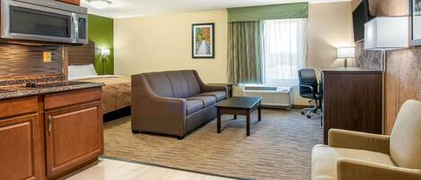 A hotel room with a kitchenette, a sofa, a bed, a desk, and a TV.