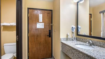 A hotel bathroom with a wooden door, a white toilet, a granite sink, and a mirror.