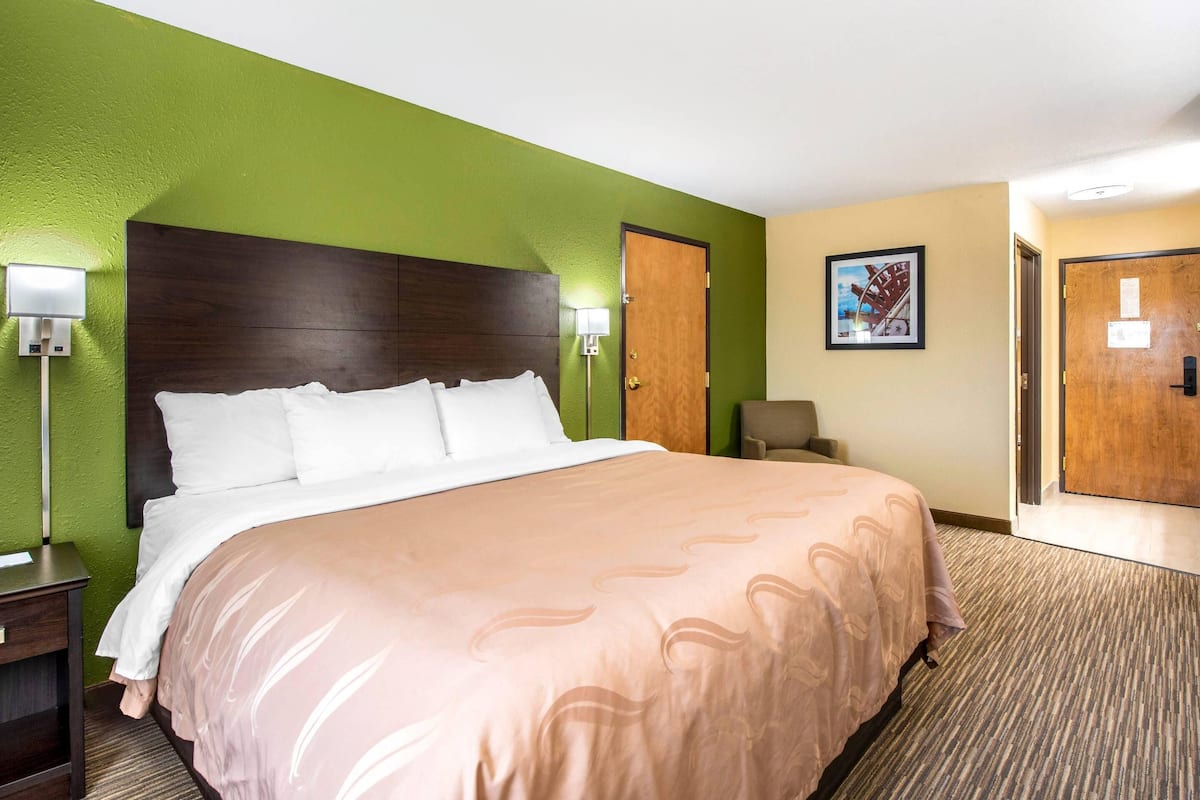 Een hotelkamer met een groot bed, groene wanden, een houten hoofdeinde en een vloerbedekking.