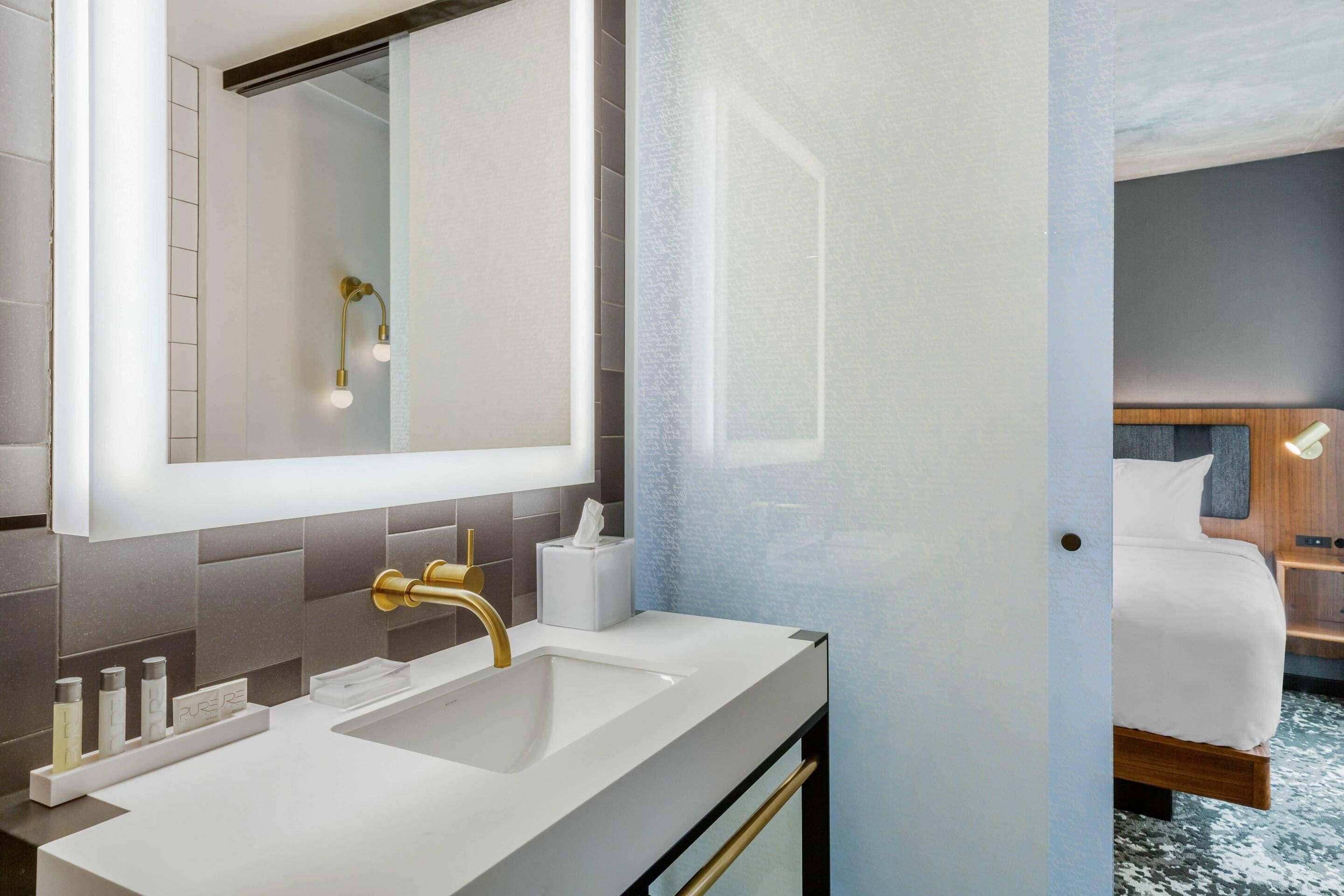 A modern bathroom with a large mirror, a gold faucet, and a white sink.