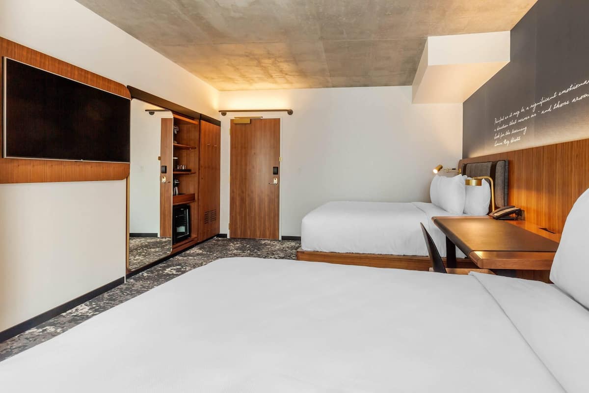 Habitación de hotel con cama, escritorio, armario y televisión de pared.