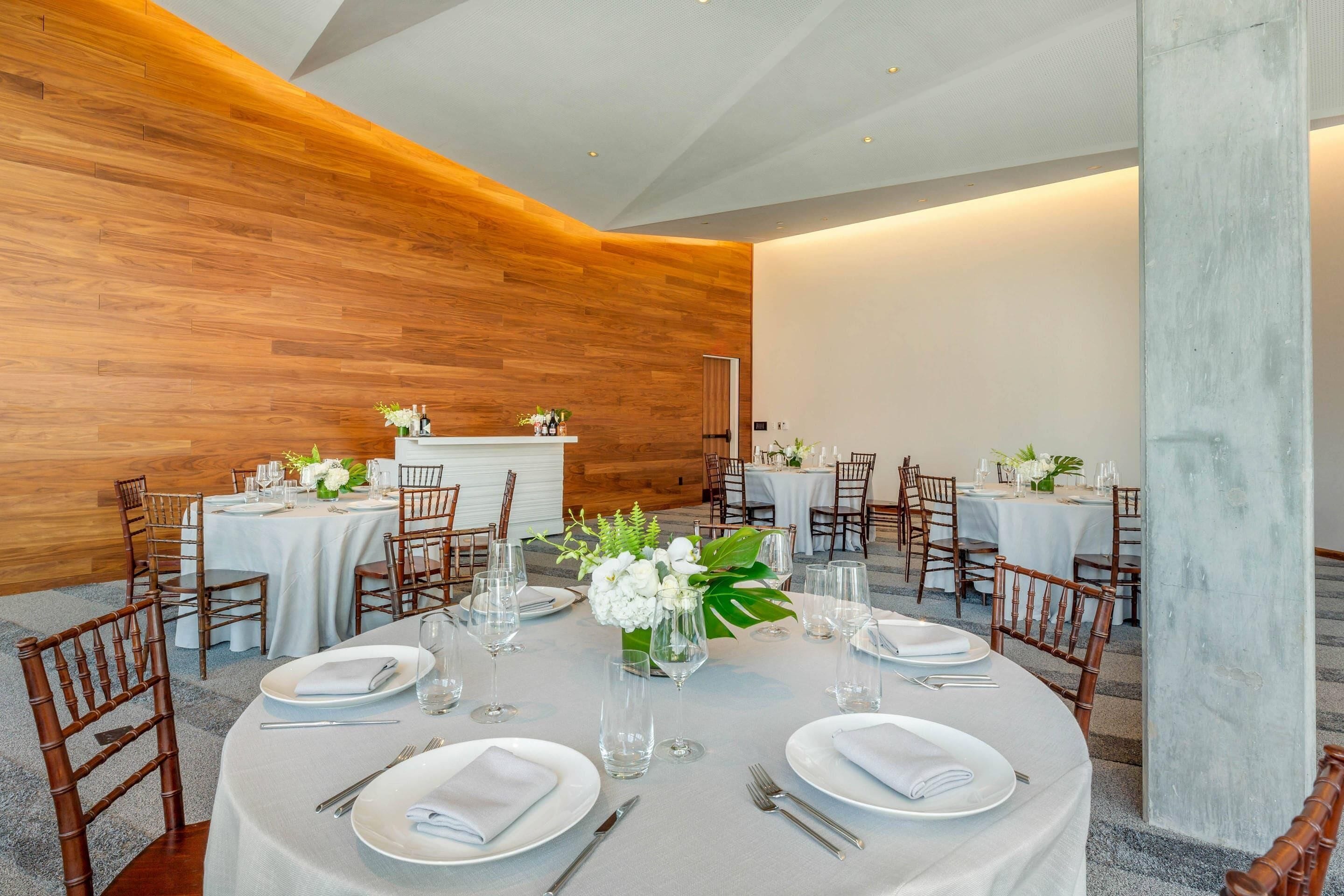 Un espace repas avec des tables rondes, des chaises et un mur décoratif en bois.