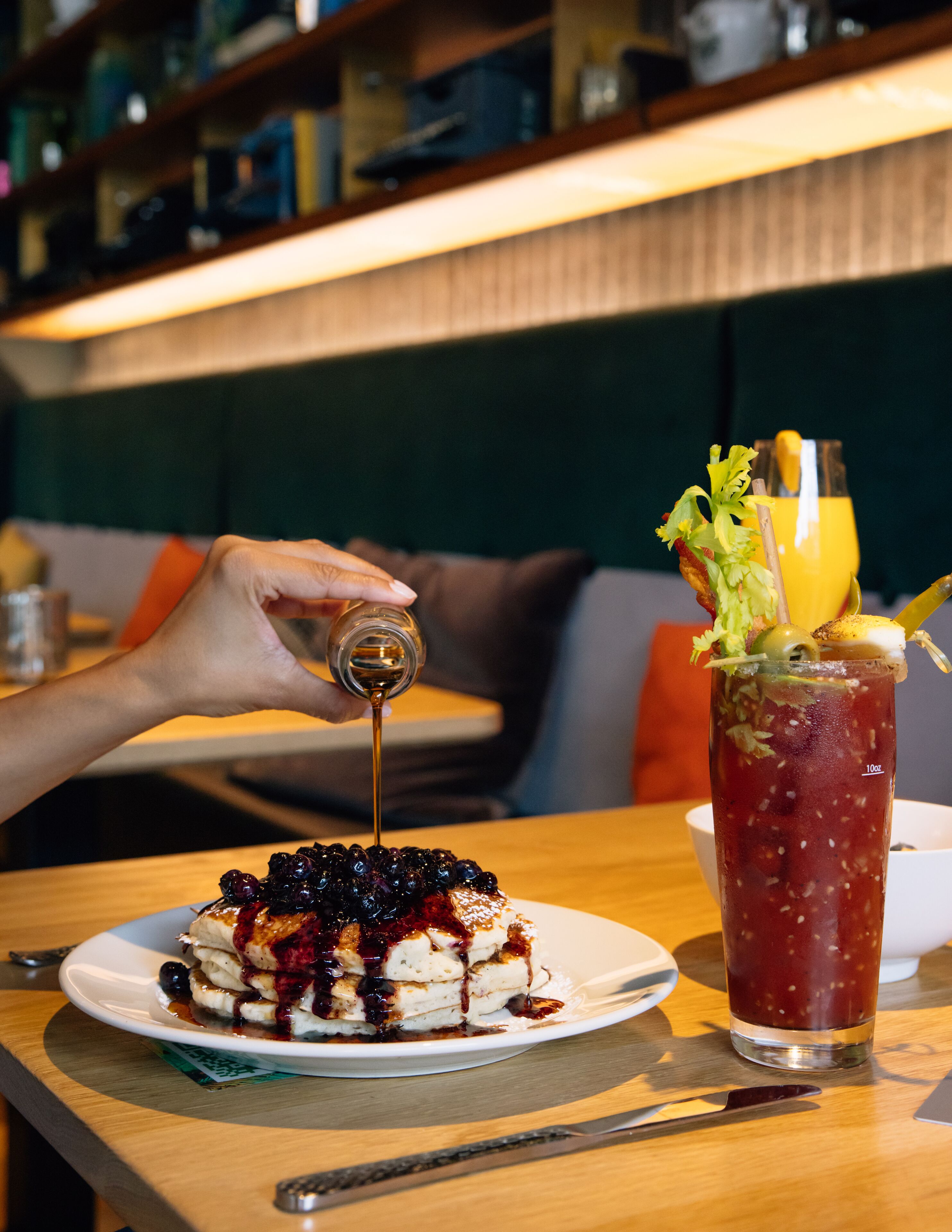 A dessert with berries and syrup on a plate, a drink with a garnish, and a hand pouring syrup.