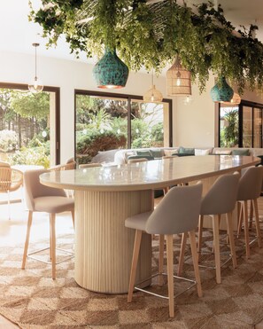 Un comedor moderno con una gran mesa ovalada, varias sillas y plantas verdes colgantes.