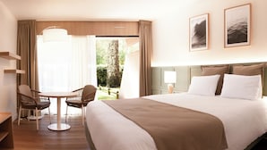 Habitación de hotel con una cama grande, un escritorio con sillas, vistas al exterior y cuadros en la pared.