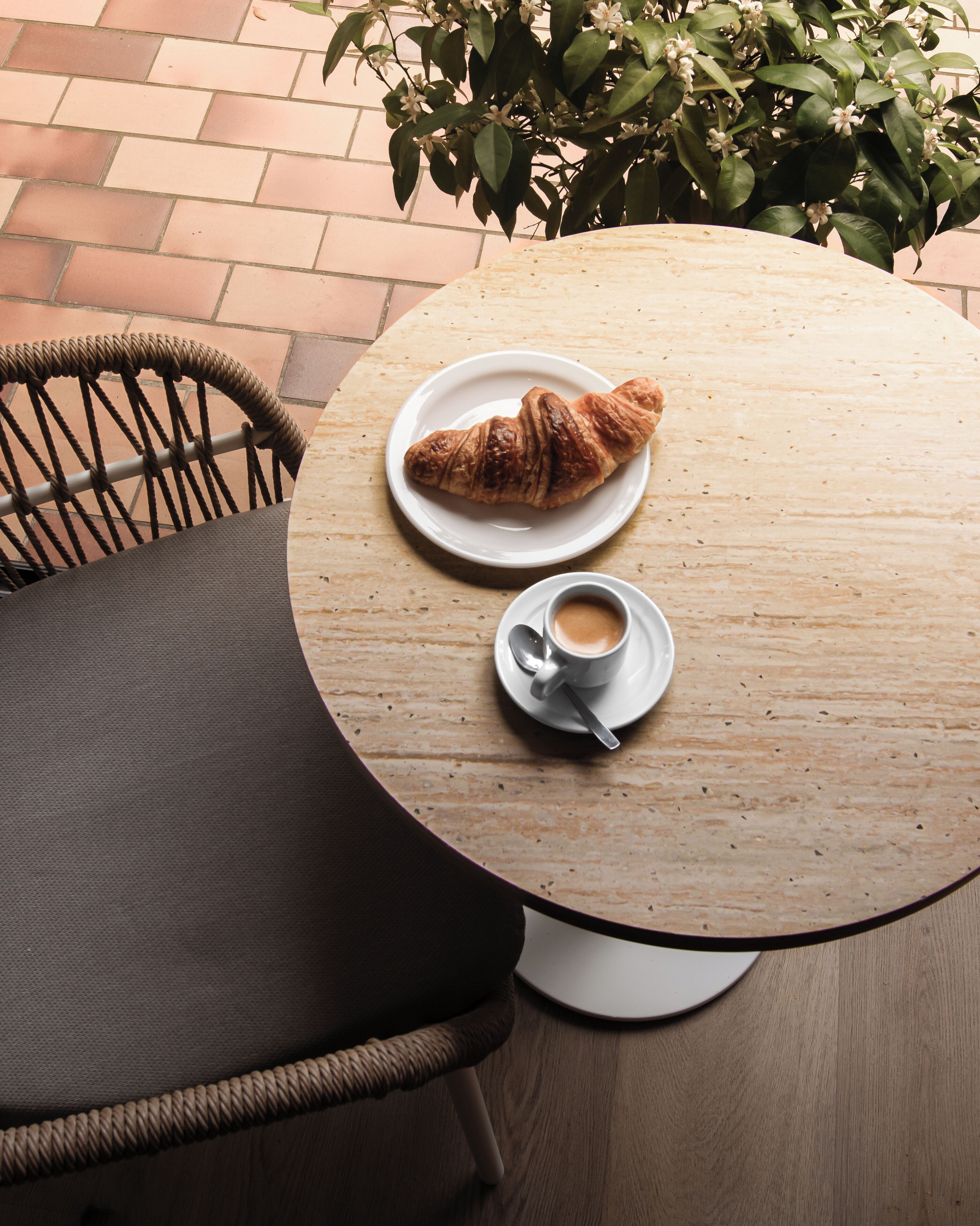 A round wooden table with a plate of croissant and a cup of coffee.