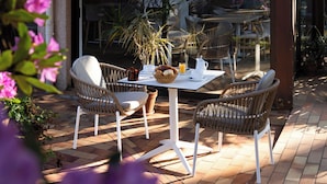 Un patio exterior con una mesa y sillas, rodeado de macetas con plantas y flores.