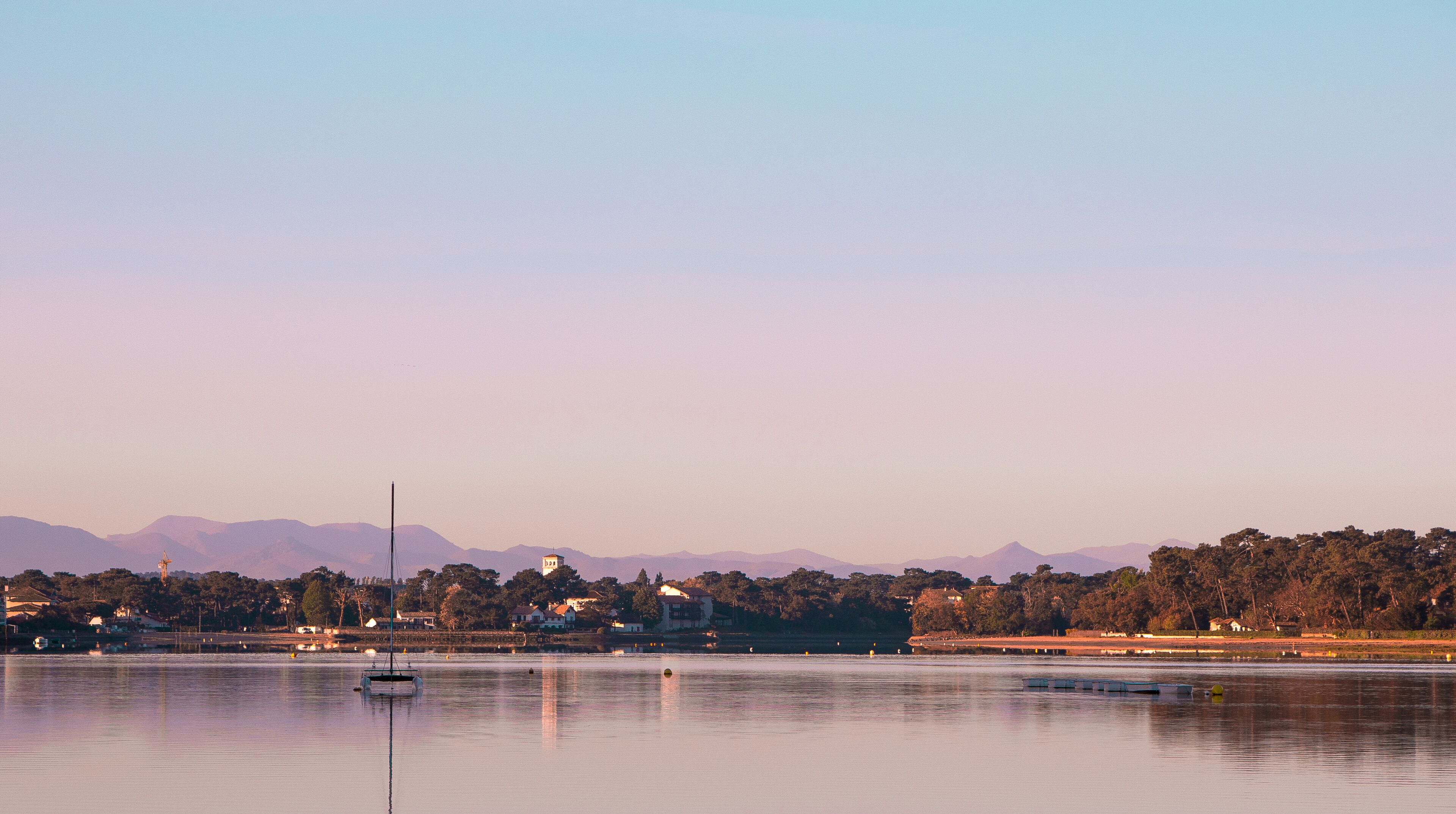 Un lac paisible, avec un voilier, un phare et des montagnes qui se dessinent à l’horizon.