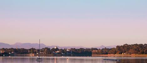 A calm lake with a sailboat, a lighthouse, and distant mountains.