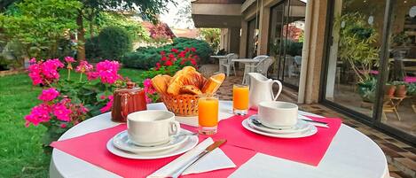 A breakfast table set outdoors with croissants, coffee, juice, and a pitcher.