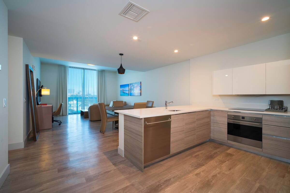 A modern kitchen with a central island, a dining area with a table and chairs, and a view of the city through large windows.