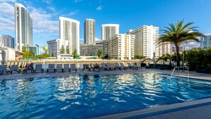 Piscina com espreguiçadeiras e um horizonte urbano ao fundo.