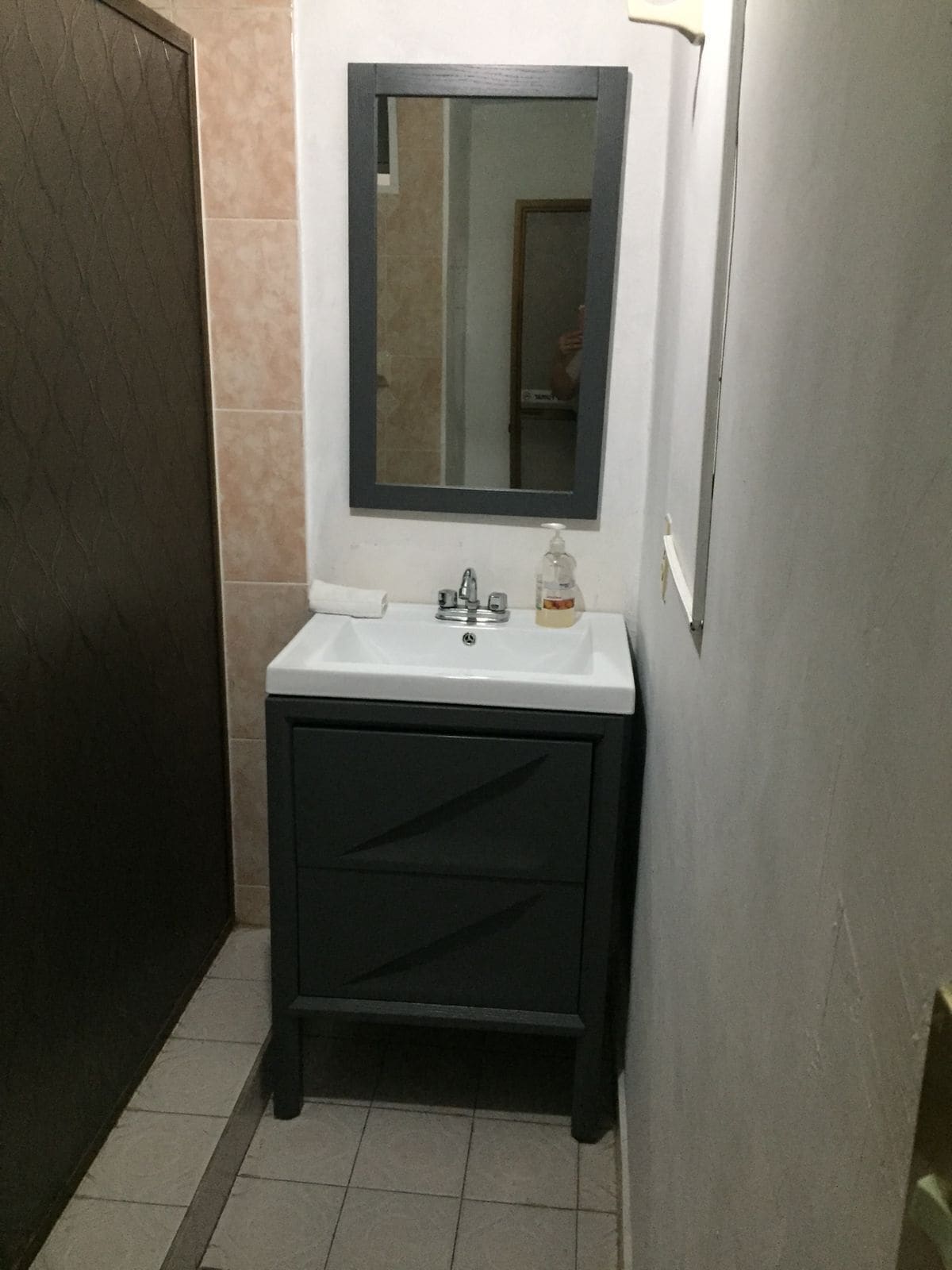 Un baño con lavamanos blanco, tocador oscuro y espejo sobre el lavamanos.