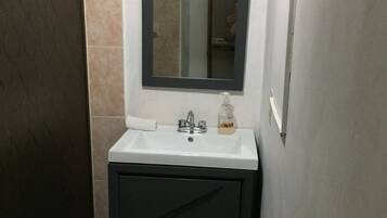 Un baño con lavamanos blanco, tocador oscuro y espejo sobre el lavamanos.