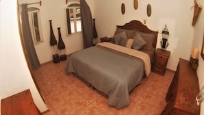A bedroom with a bed, nightstands, a wooden dresser, a ceiling fan, and a window with curtains. - Hostal Casa Blanca (Comala)