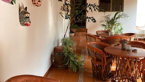 A cozy dining area with wicker furniture and a variety of colorful masks on the wall. - Hostal Casa Blanca (Comala)
