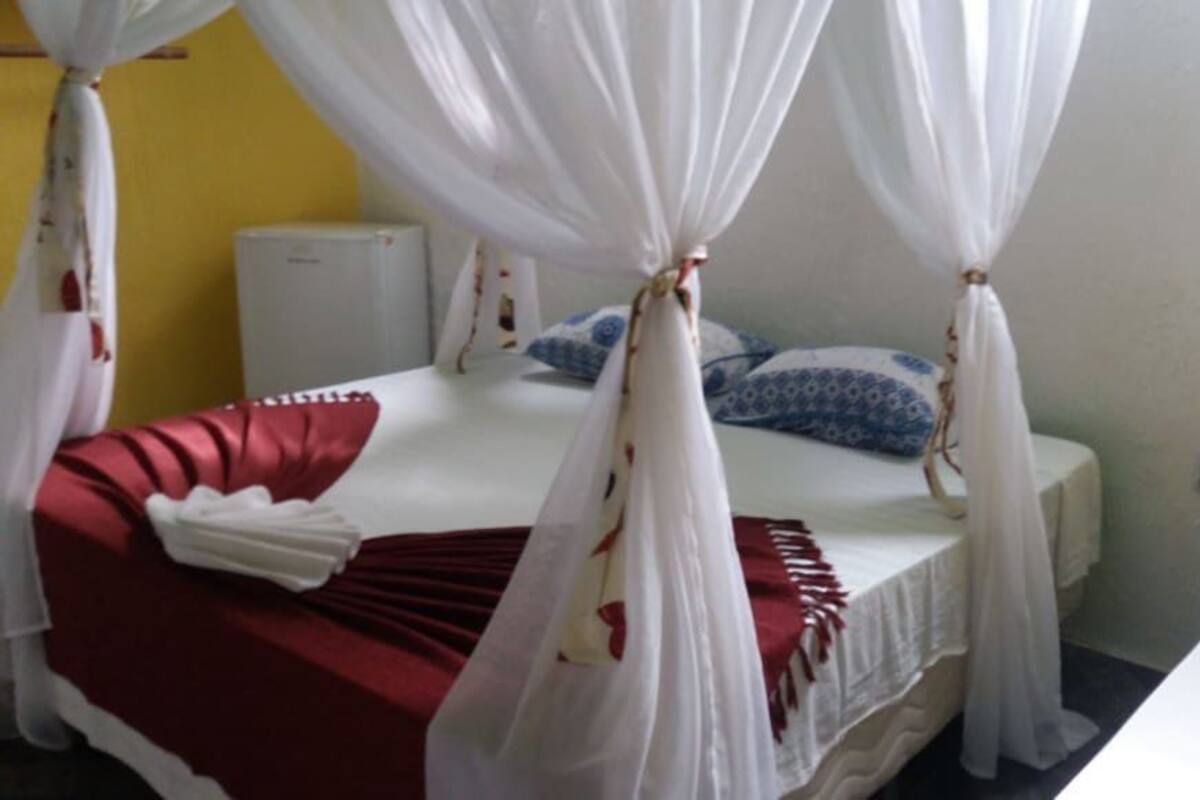 A single bed with a red bedspread, white curtains, and a white canopy.