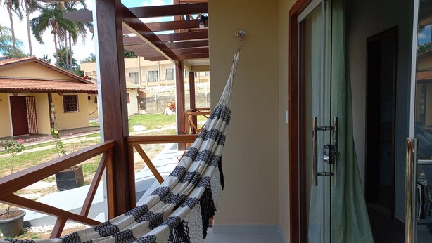 A hammock hanging on a balcony with a view of a building and palm trees. - Pousada Aconchego da Chapada (Alto Paraíso de Goiás)