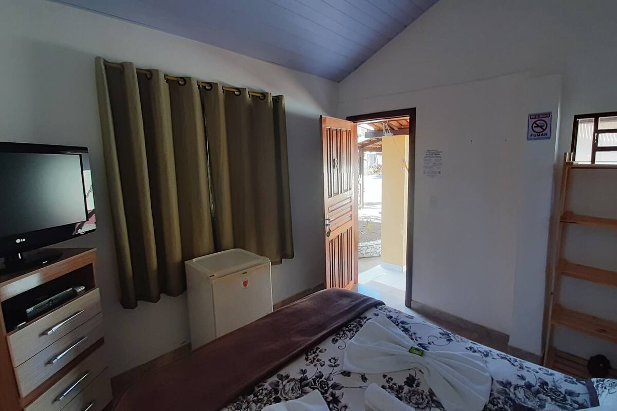 A bedroom with a bed, a TV, a wardrobe, a small cabinet, and a door leading to an outdoor area.