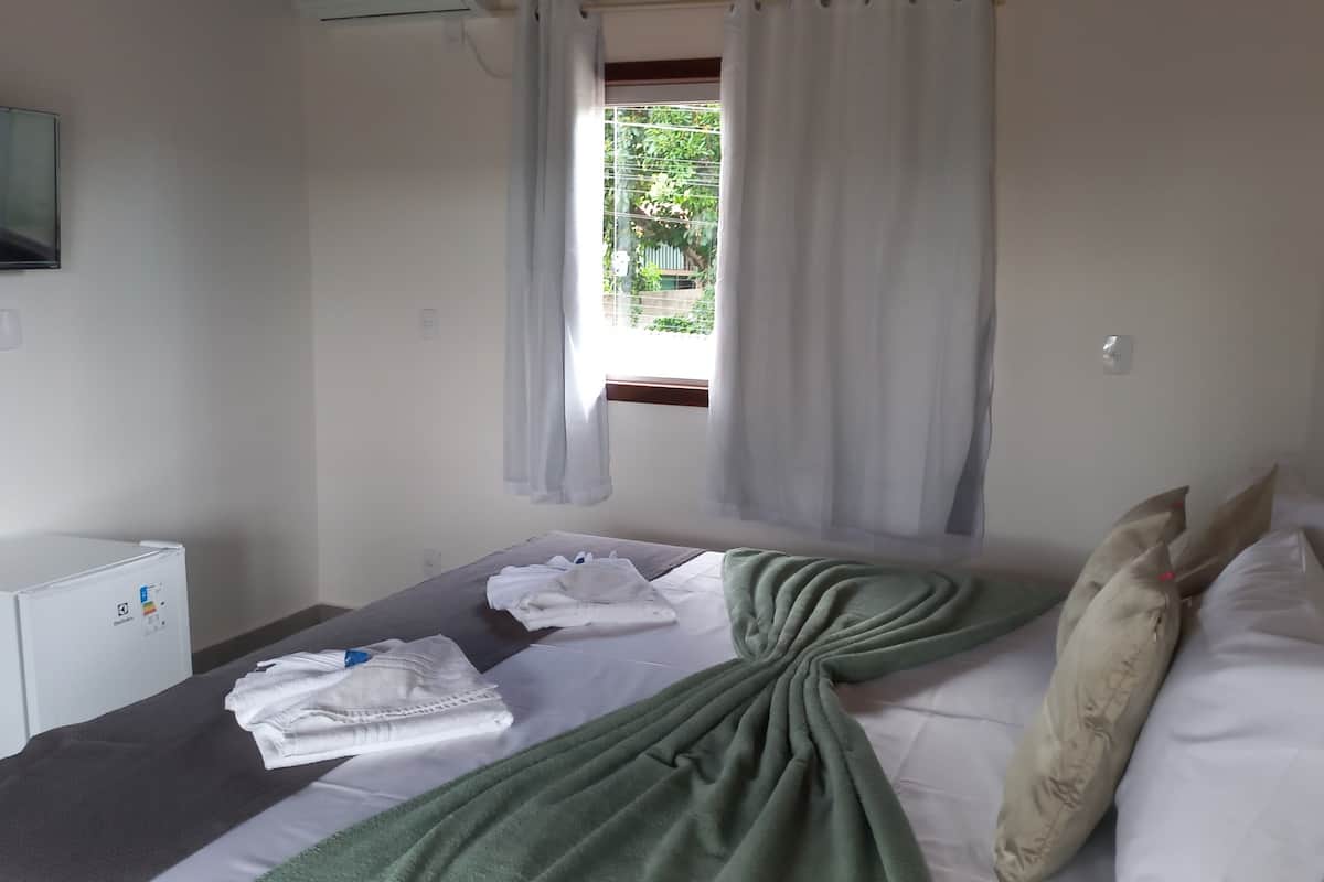 A hotel room with a bed, a TV, a desk, and a window with curtains.