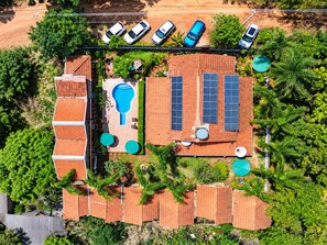 An aerial view of a residential property with a swimming pool, solar panels, and a fenced garden area. - Pousada Quinta Dos Quintais (Chapada dos Guimarães)