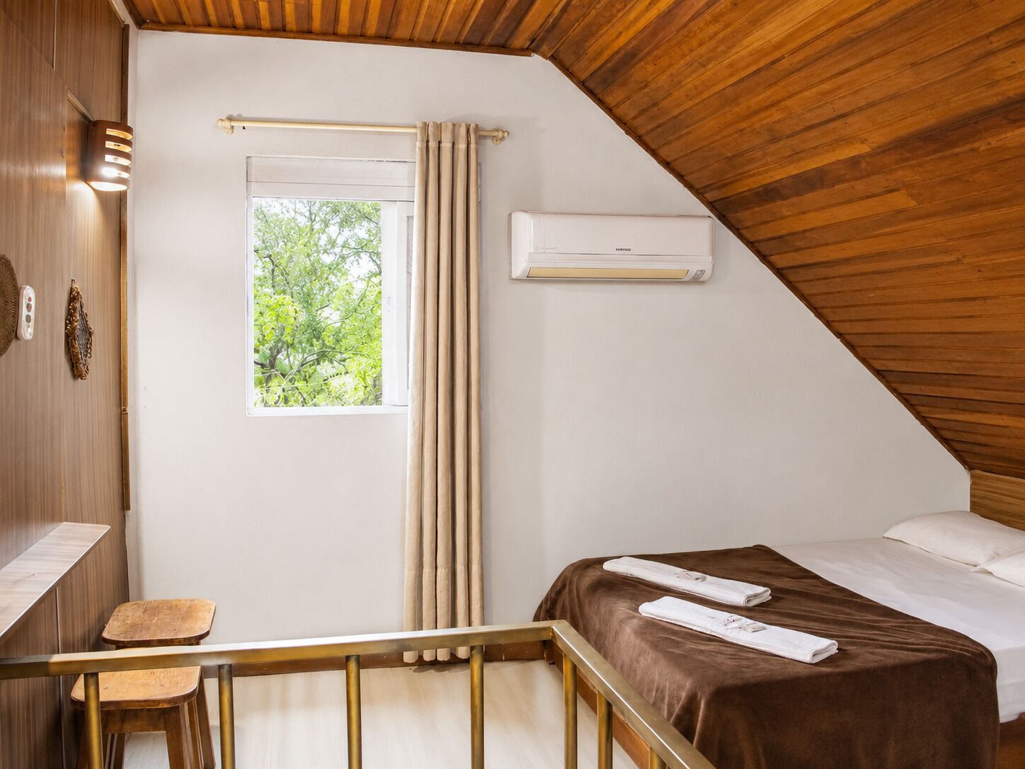 Una habitación con cama, ventana con cortinas, unidad de aire acondicionado y techo de madera.