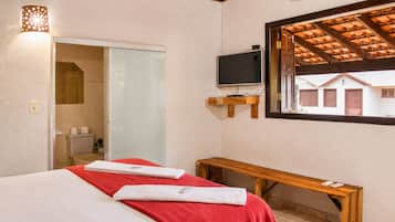 Habitación de hotel con cama, televisor, banco y ventana con vista a edificios.