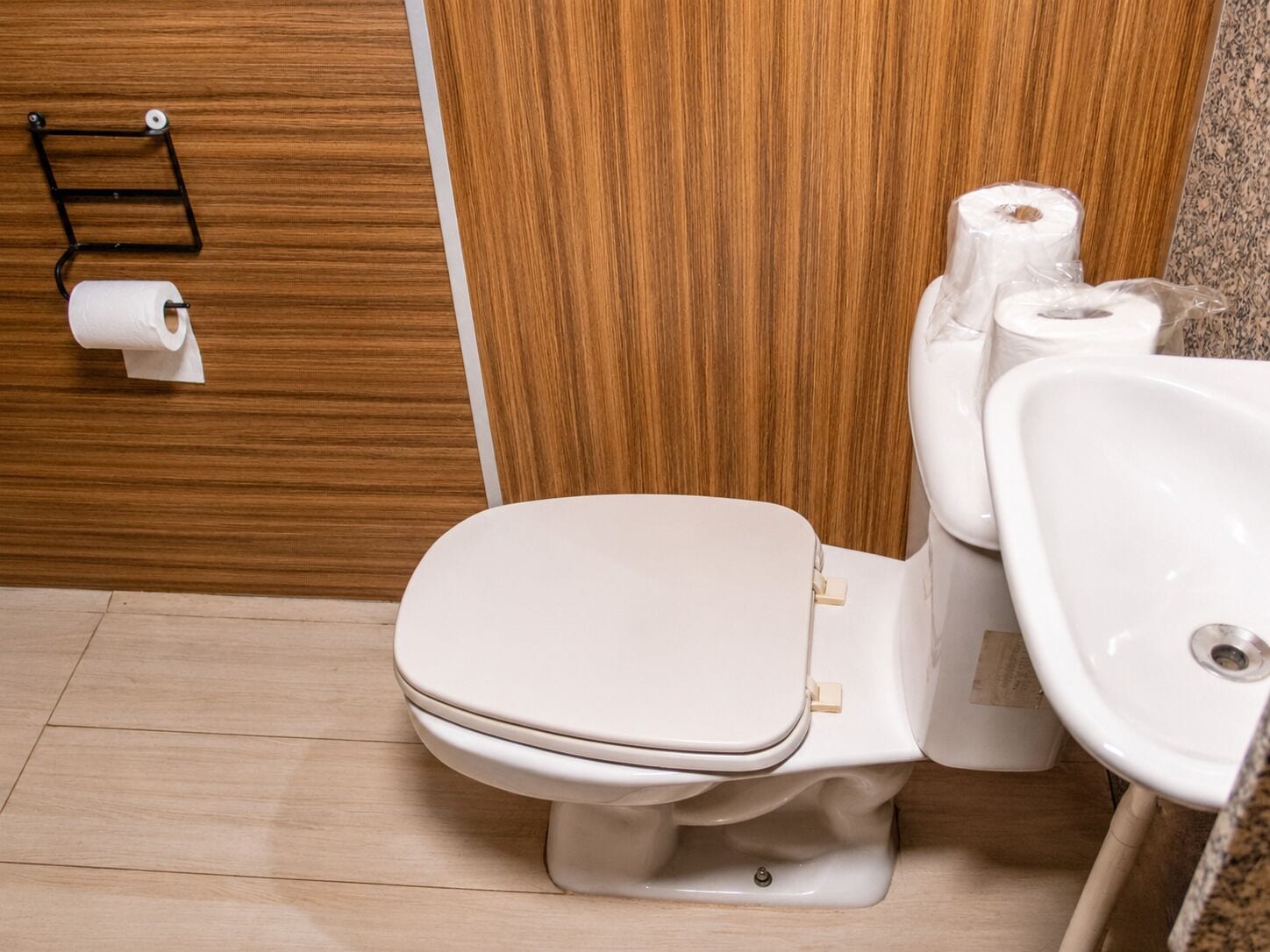 A modern bathroom with a toilet, sink, and wooden wall.