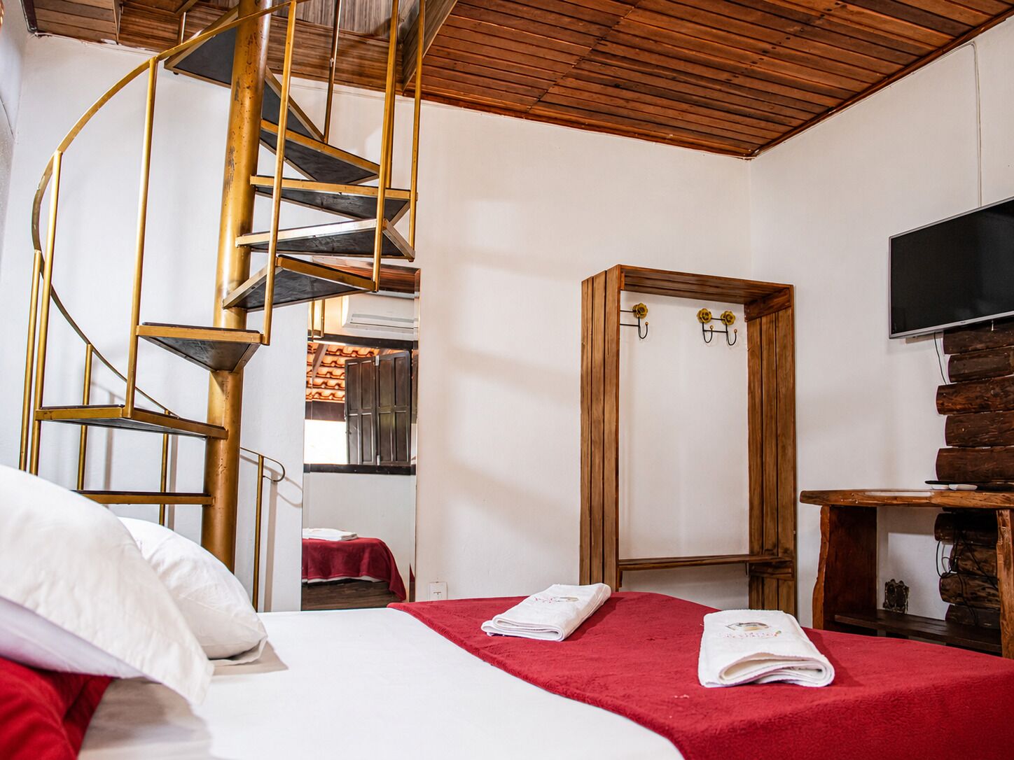 Habitación de hotel con escalera espiral, armario de madera, cama con ropa de cama roja y televisor de pantalla plana.