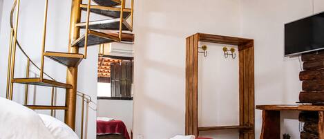 Habitación de hotel con escalera espiral, armario de madera, cama con ropa de cama roja y televisor de pantalla plana.