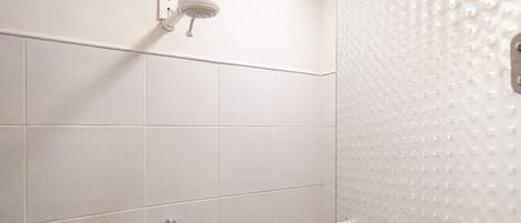 Ducha con cabezal de ducha de mano, grifería de control visible y puerta de ducha texturizada.