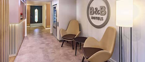 A hotel reception area with a B&B sign, two leather chairs, a floor lamp, and a reception desk.