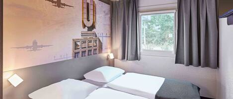 Habitación de hotel con dos camas, una ventana con cortinas, un mural en la pared y una mesita.