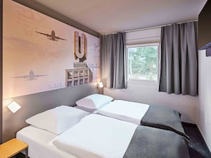 A hotel room with two beds, a window with curtains, a wall mural, and a small table. -  B&B HOTEL Dortmund-Airport (Holzwickede)