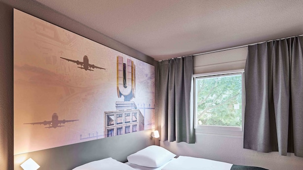 Une chambre d’hôtel avec un lit, une table de chevet, une fenêtre avec des rideaux et un mur orné d’une fresque.