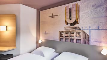 A hotel room with a large bed, two bedside tables, and a wall mural depicting a cityscape with a large 'U' structure.