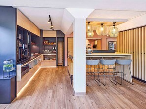 A modern kitchen with a bar area, wooden flooring, and pendant lighting. -  B&B HOTEL Dortmund-Airport (Holzwickede)
