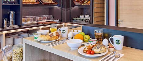 Ein Frühstücksbuffet mit verschiedenen Speisen, einer Kaffeemaschine und einem Kühlschrank mit Getränken.