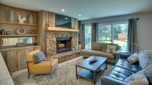 A cozy living room with a stone fireplace, comfortable seating, and a large window offering a view of the outdoors. - Walk to Beaver Creek Shuttle! Avon Condo w/ Deck (Avon)